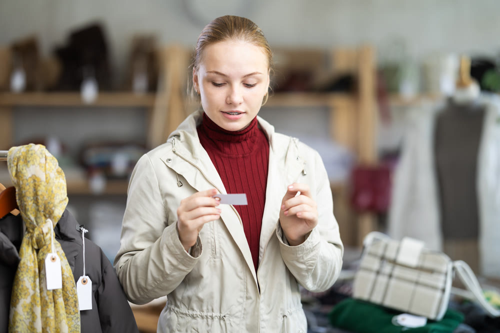 Selective teenage girl trying on beige jacket in clothing store
