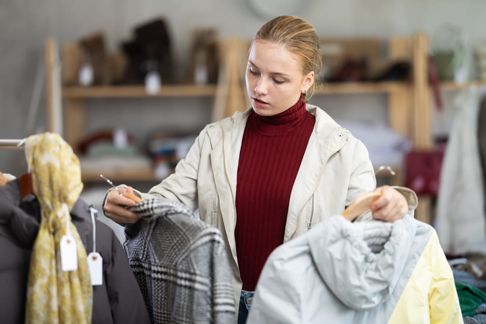 Attentive teenage girl choosing lightweight jacket in clothing store