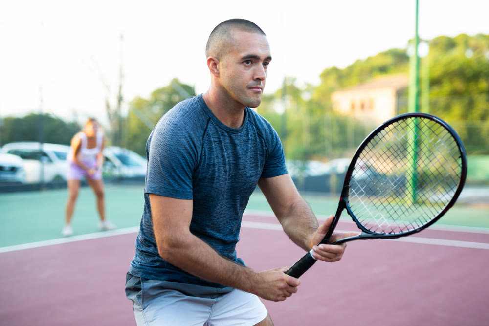 Portrait of sporty man standing with tennis racquet in his hands ready to play match in open court