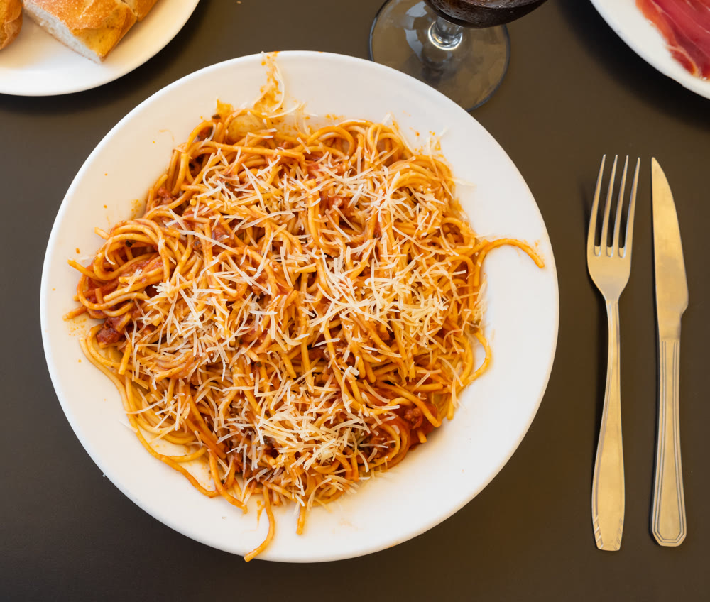 Delicious noodles Bolognese served with grated parmesan in plate with table appointments