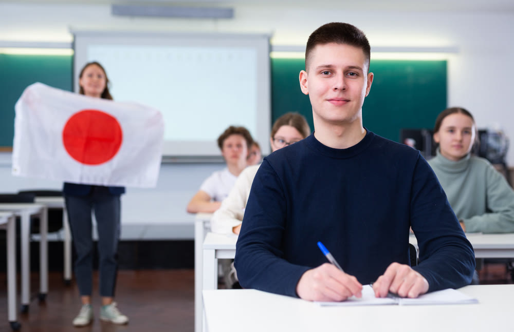 High school teacher tells students about Japan and holds a Japanese flag in hands.