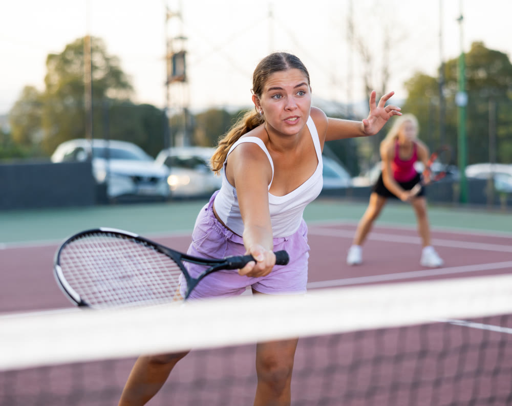 Positive female player hits ball close to net while playing tennis