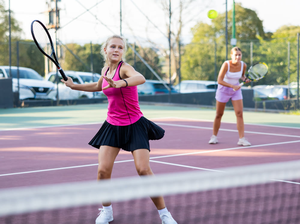 Sportive woman dressed in t-shirt and skirt playing tennis with partner