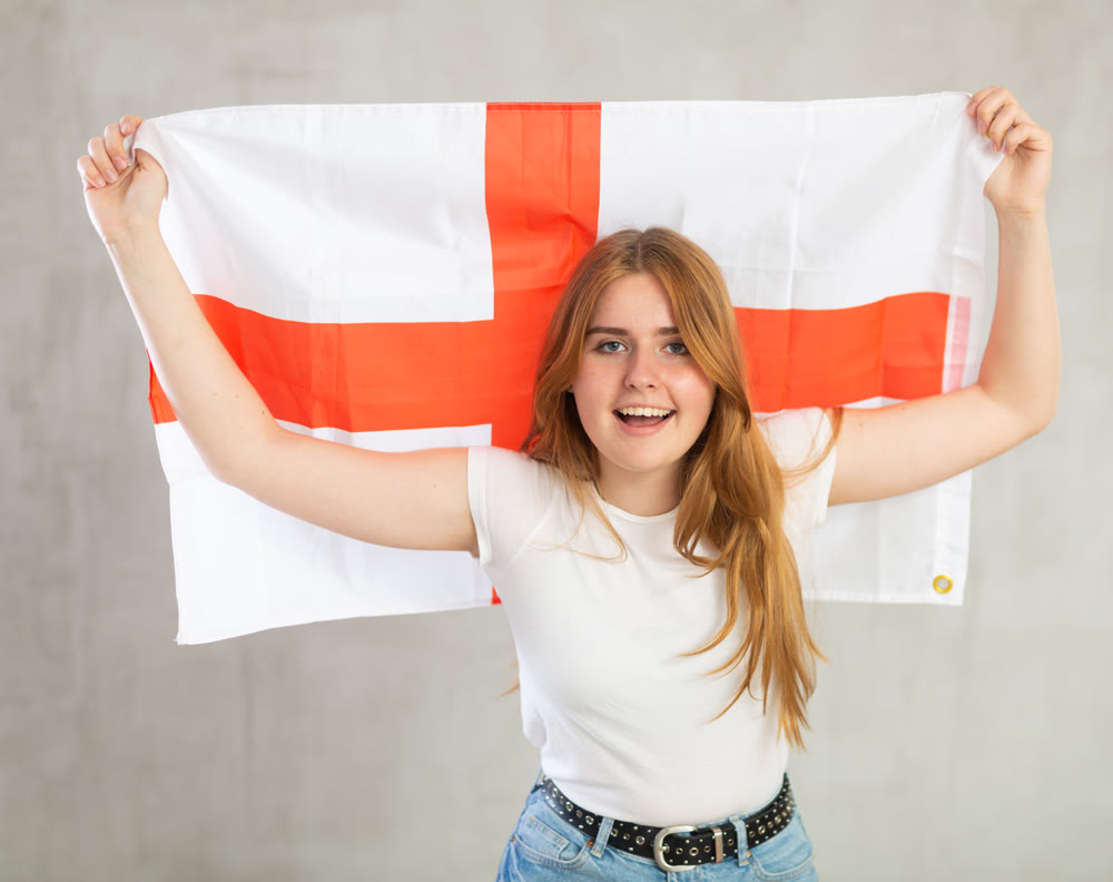 smiling girl in arms raised above head holds canvas of national flag of England