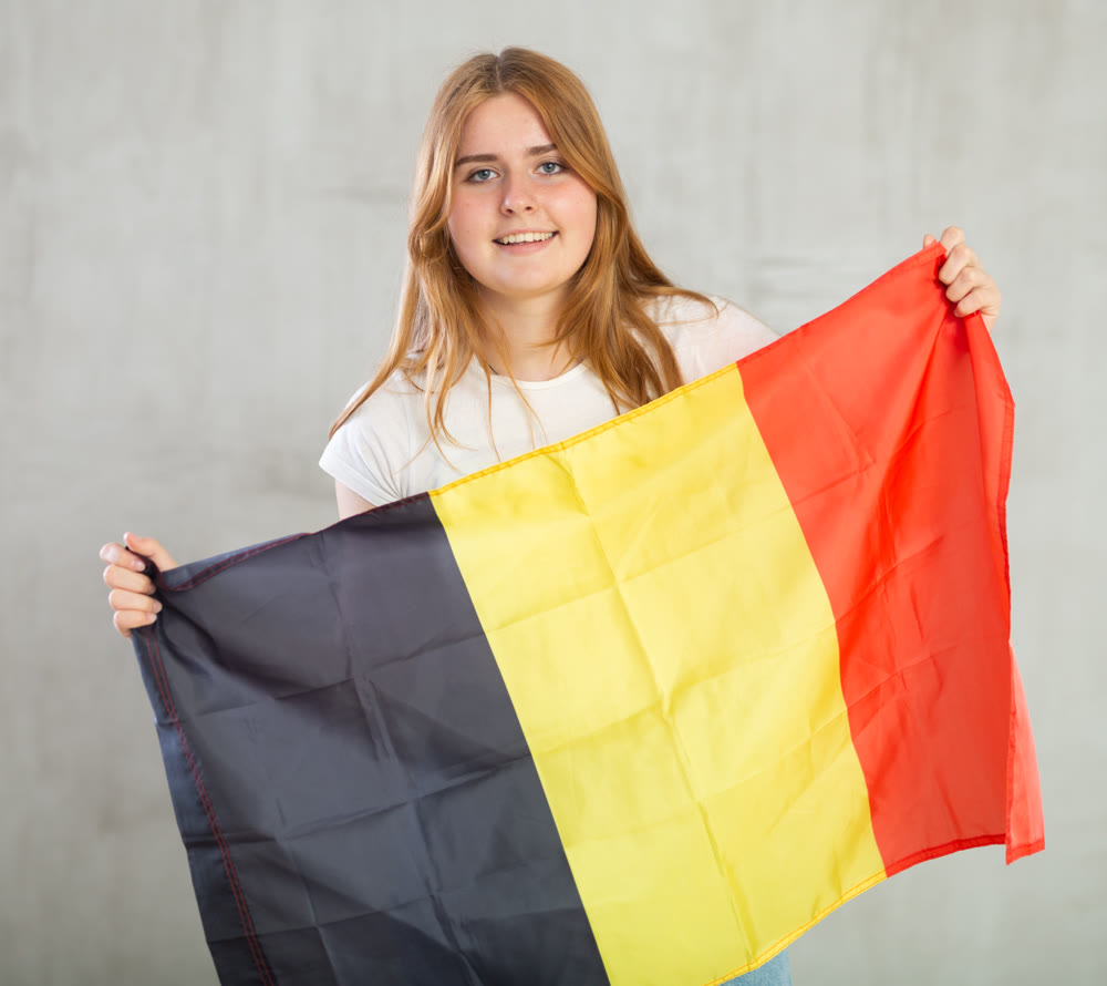 smiling girl in arms raised above head holds canvas of national flag of Belgium.