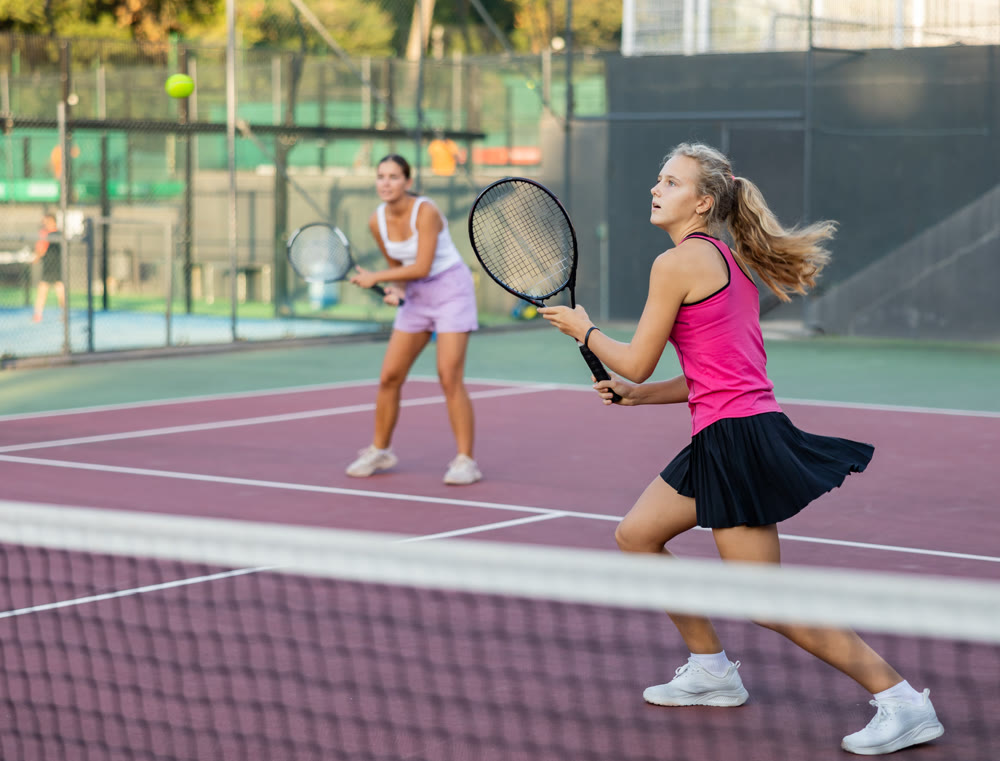 Sports active woman during friendly doubles couple match. Two women playing together tennis