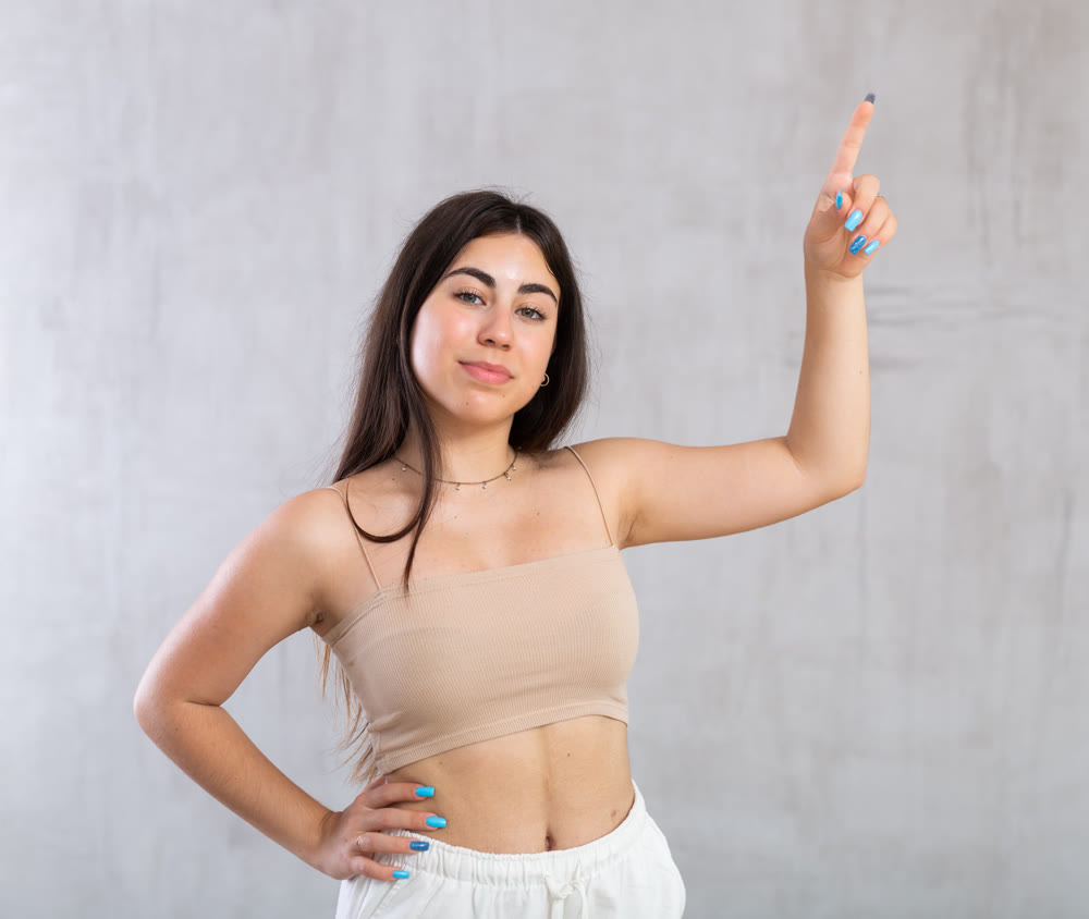 Young woman pointing up standing against the wall