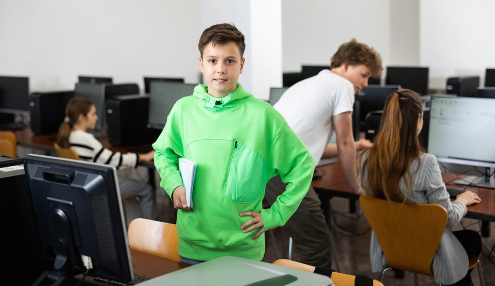 Preteen schoolboy with workbooks in hands standing in computer class