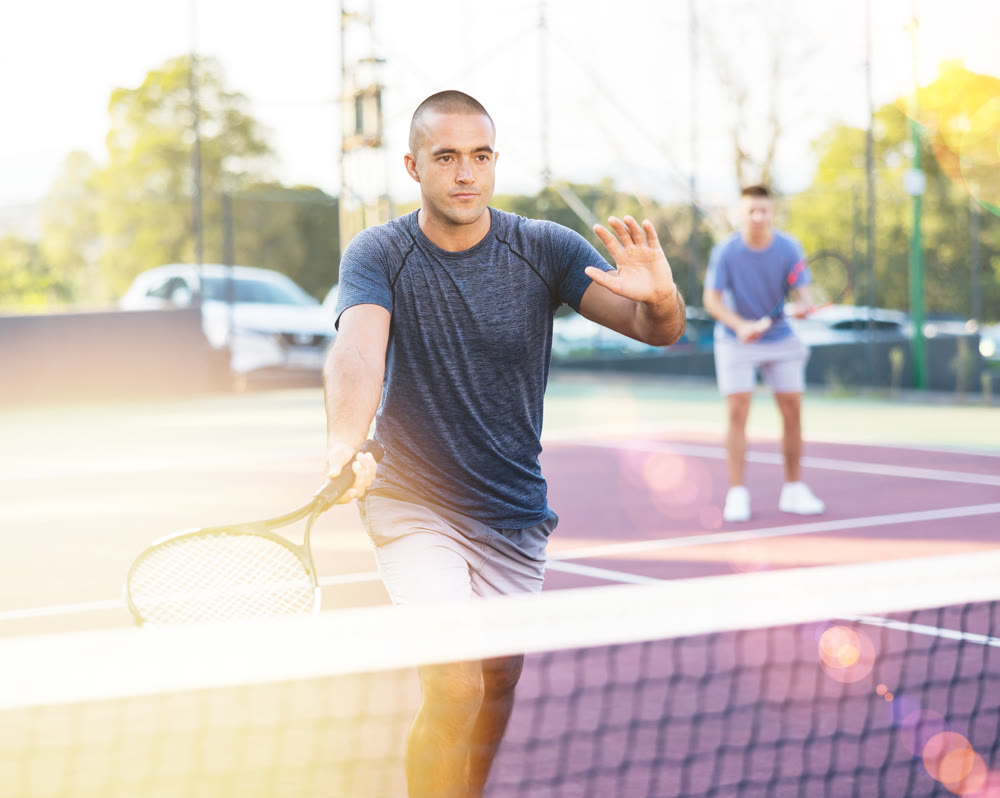 Young man and his male partner playing tennis on court during friendly match