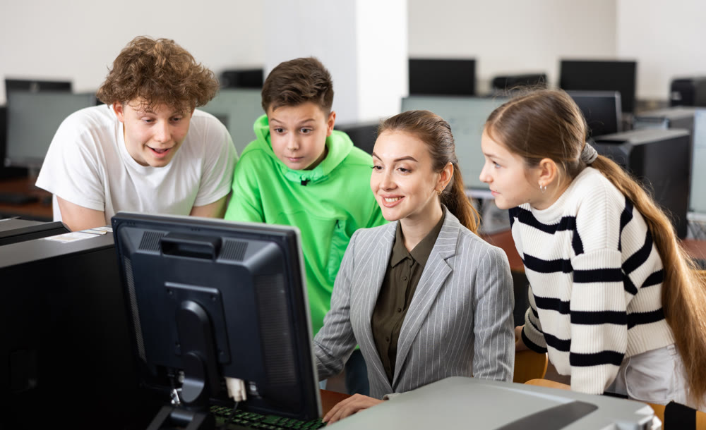 Female teacher helping schoolboy and schoo lgirl in computer class