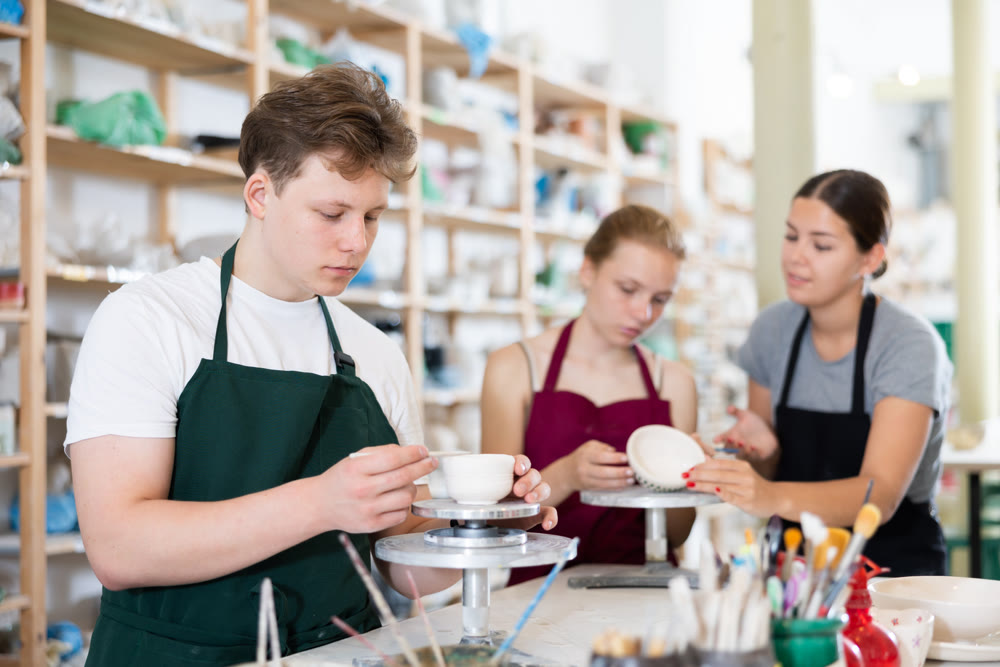 Young man leveling the edges of pottery with wooden stick