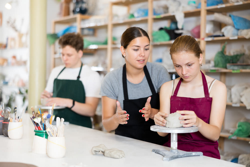 Young woman teacher helps teenagers boy and girl to sculpt ceramic product