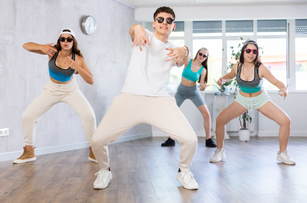 Guy and group of young girls in dark glasses and ball cap dance modern Jazz-modern in fitness club
