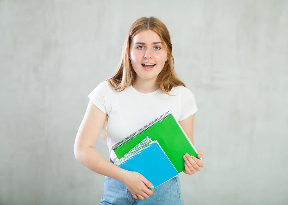 Portrait of an expressive surprised girl student with notebooks in hands