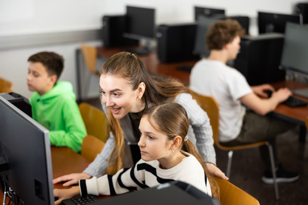Female teacher talking to focused teen girl student in computer class