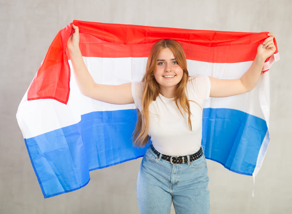 smiling girl in arms raised above head holds canvas of national flag of Netherlands