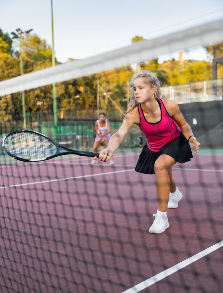 Sportive woman in shorts and t-shirt playing tennis on court. View through tennis net
