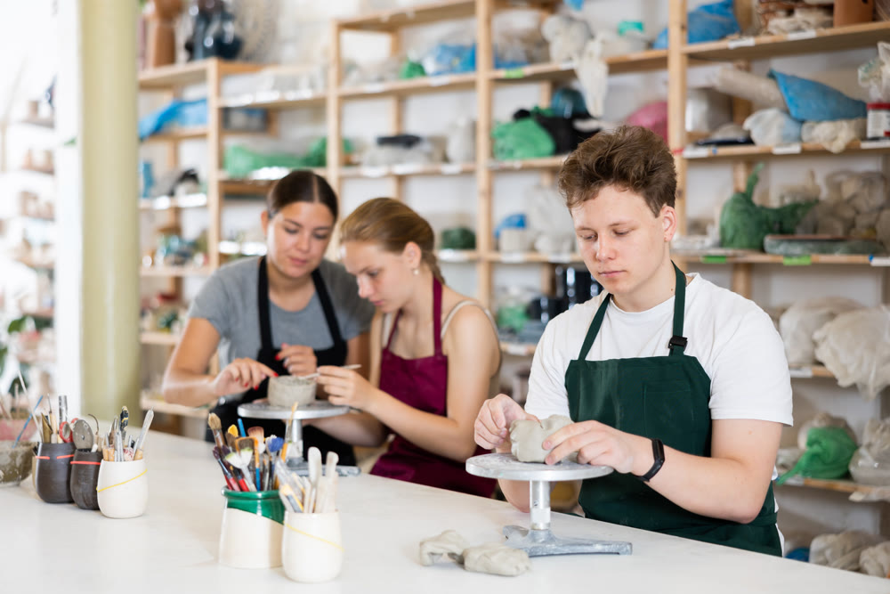 Young woman teacher helps teenagers boy and girl to sculpt ceramic product