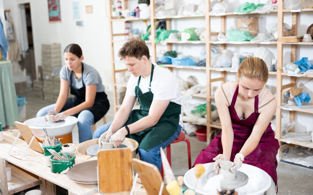 Young woman teacher and two teenagers make products on potter's wheel