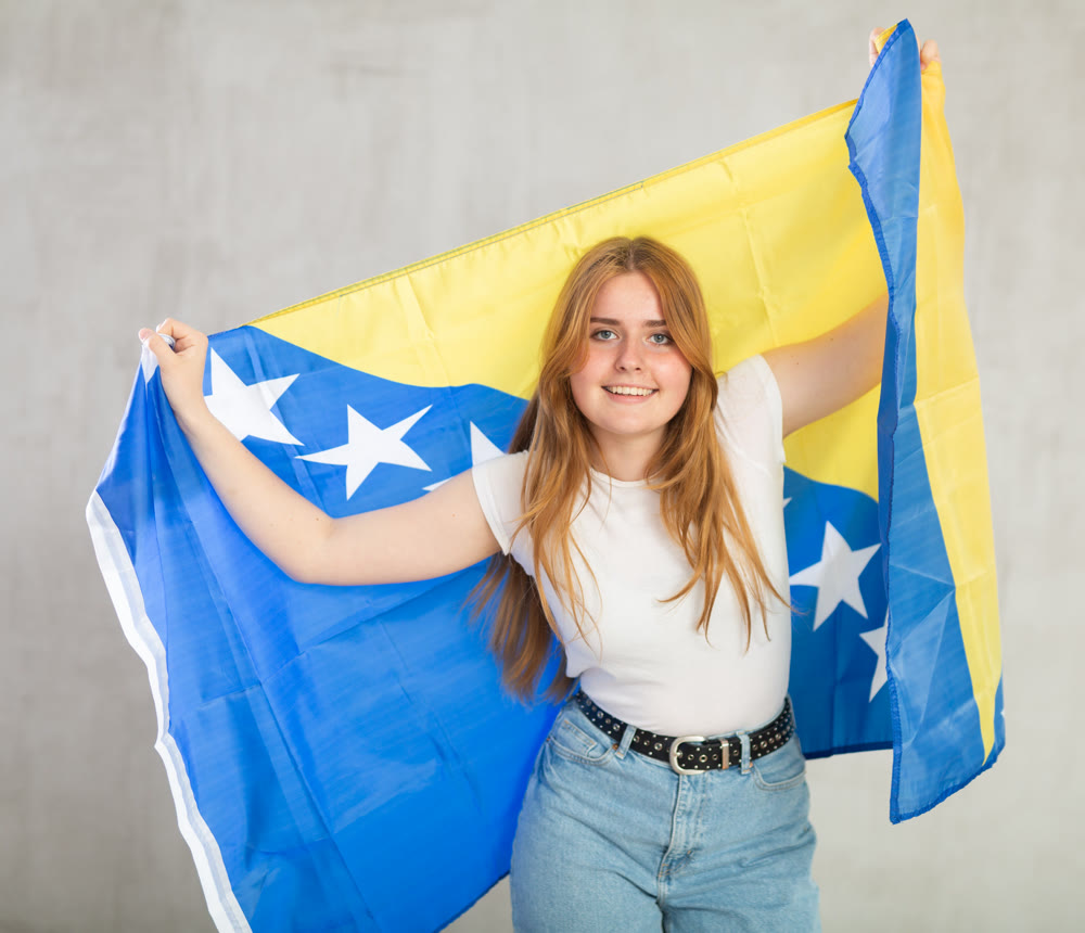 smiling girl in arms raised above head holds canvas of national Bosnian flag