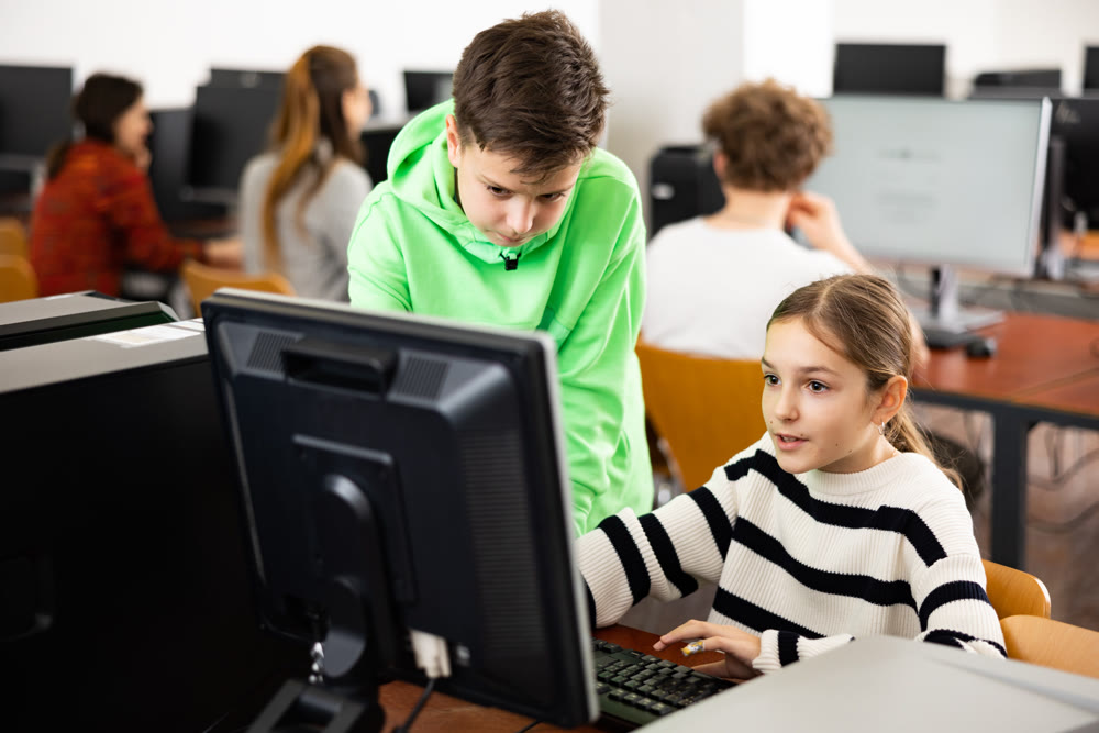 Teenager guy helps girl solve problem on computer in school class