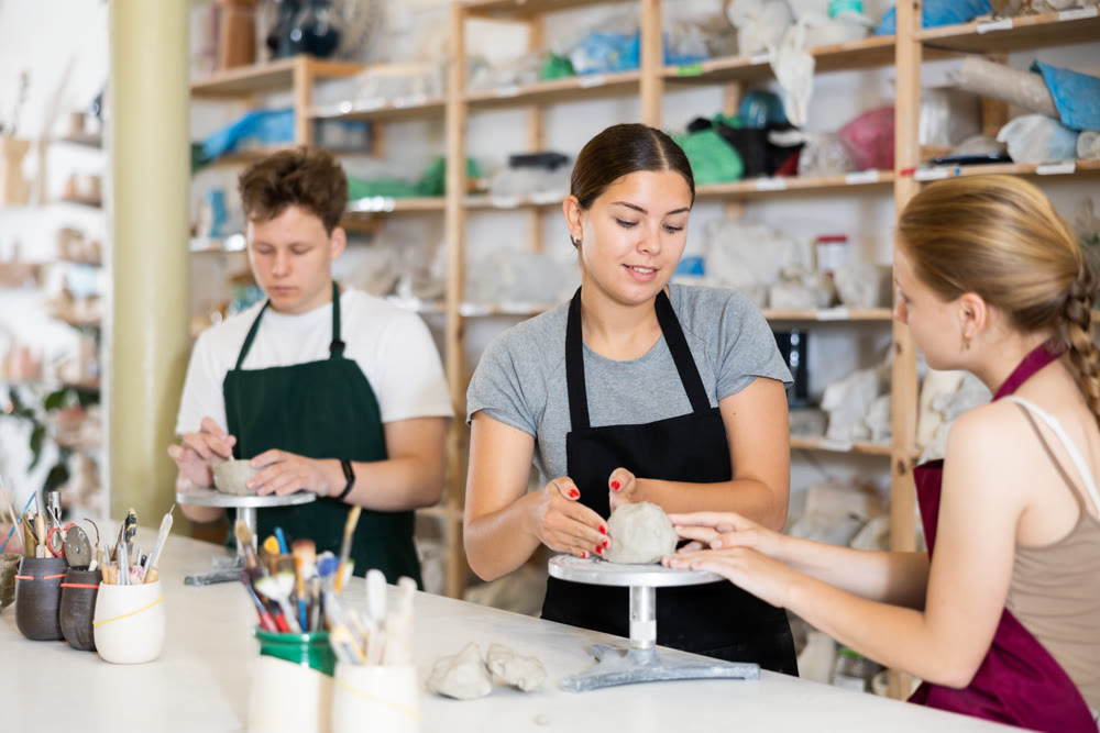 Young woman teacher helps teenagers boy and girl to sculpt ceramic product
