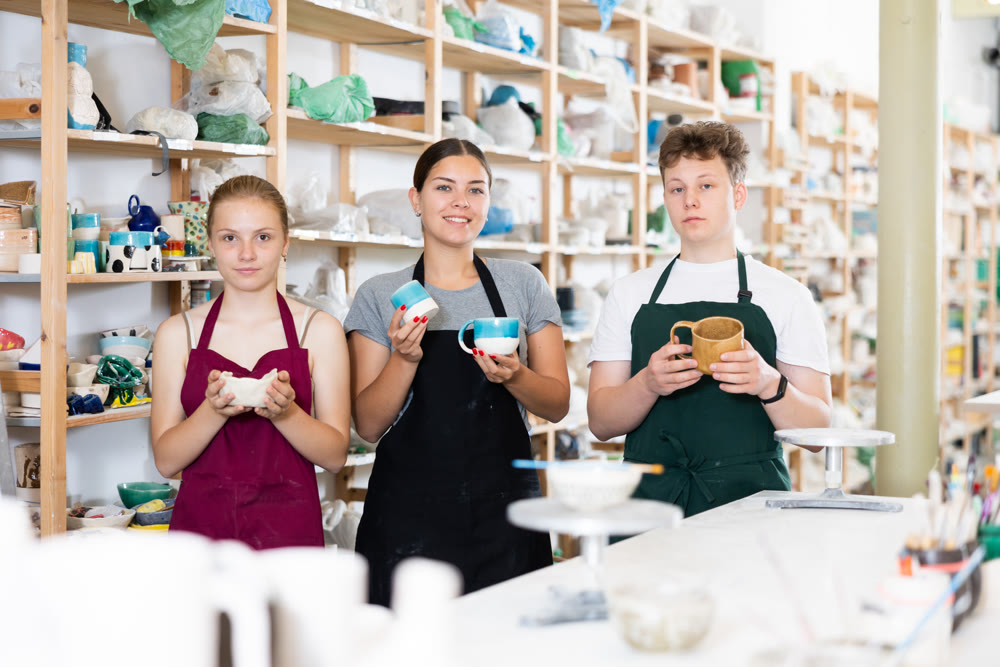 Young students, together with pottery teacher, show clay mugs they made with their own hands
