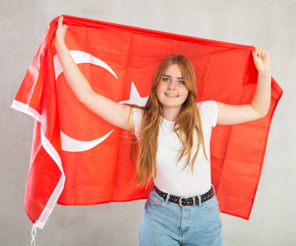 smiling girl in arms raised above head holds cloth of national flag of Turkey