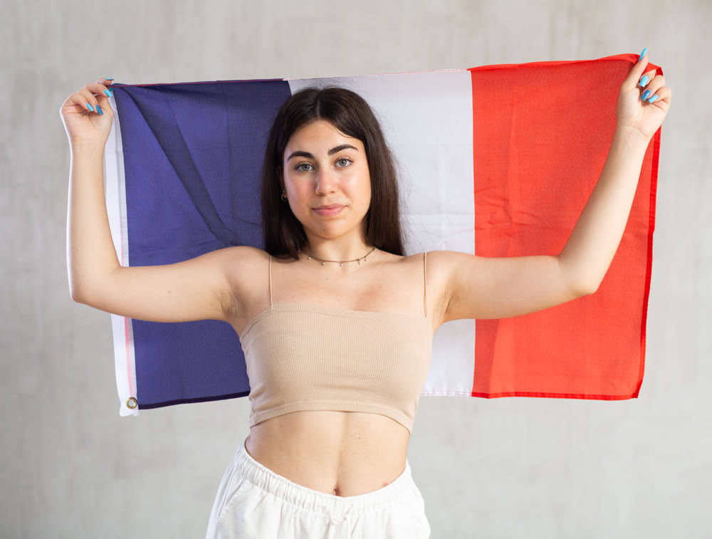 Happy young woman with flag of France against unicoloured background