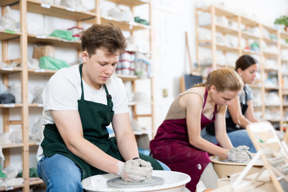Young woman teacher and two teenagers make products on potter's wheel