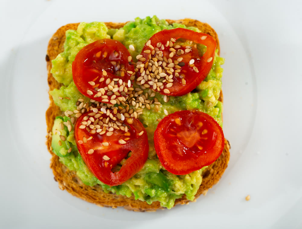 Sandwich with guacamole butter, tomatoes and seeds on whole grain bread