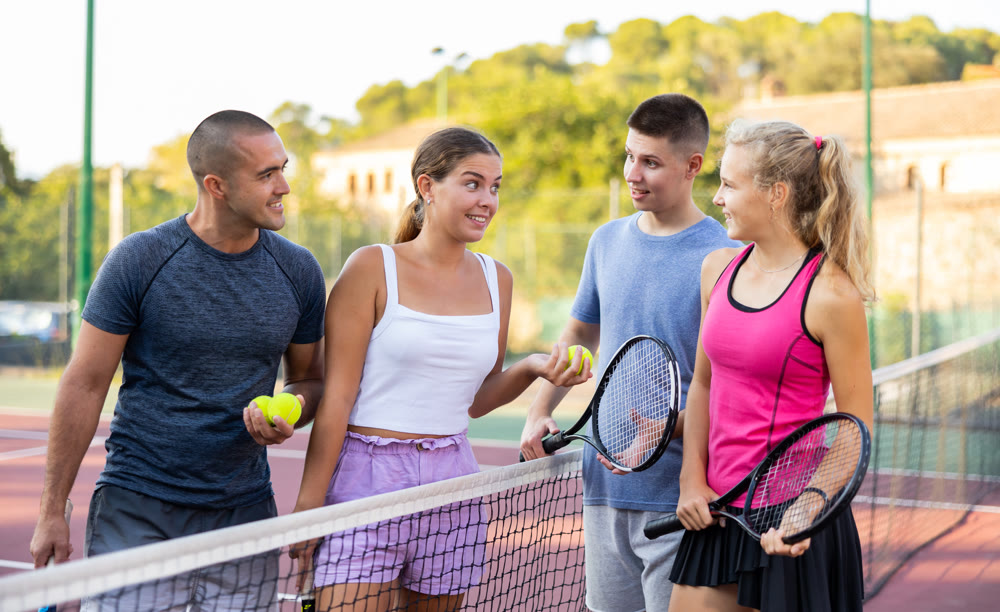Two pairs of tennis players are happily discussing past game on an open court