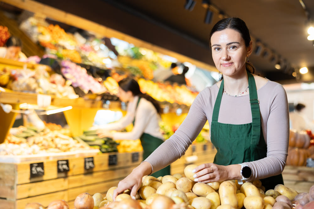 Adult woman seller puts potatoes in vegetable shop