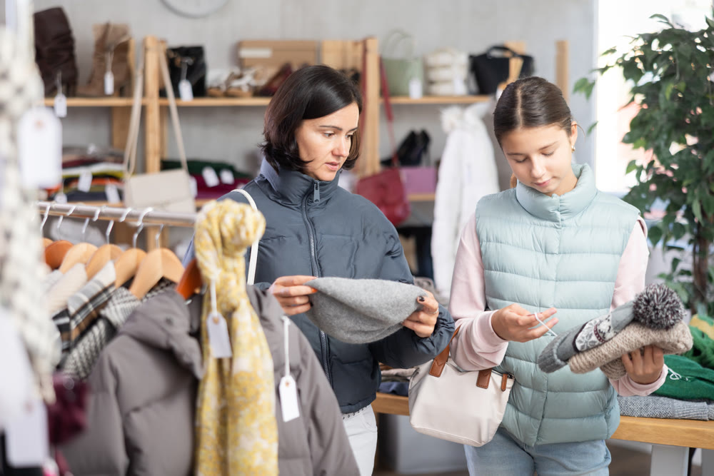 Mother and teen daughter looks at products in store and selects hat for teen child.