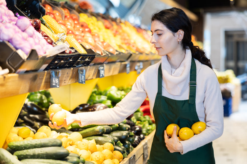 Young woman seller puts lemons in vegetable shop