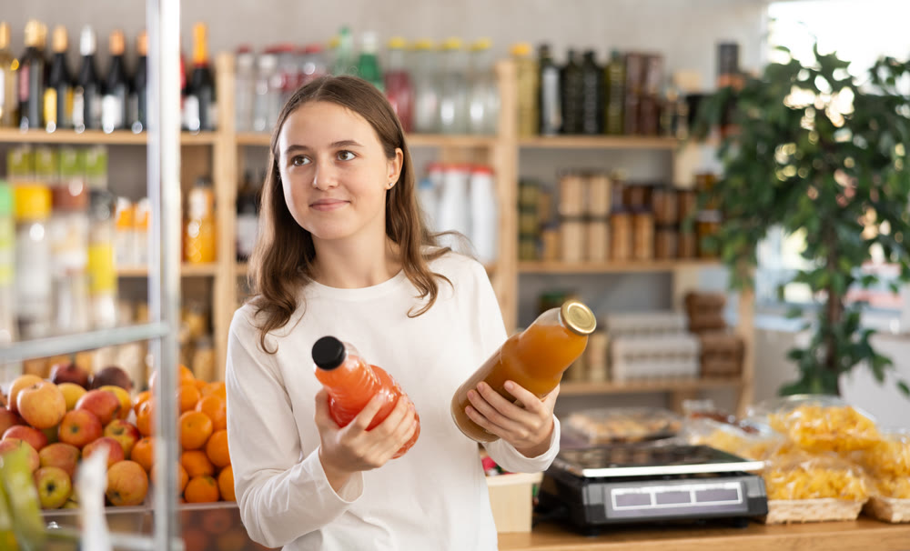 Teen girl hold packages bottles and choose consider juice in store