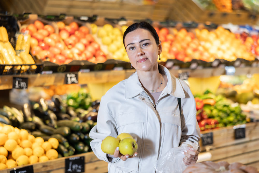 Portrait of female shopper carefully selecting ripe apples on supermarket display