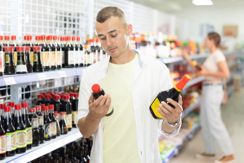 Young man choosing soy sauce in Asian food store