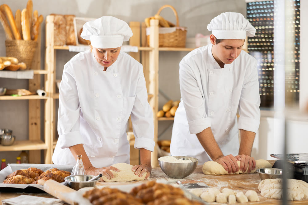 Two chefs knead dough and communicate while working