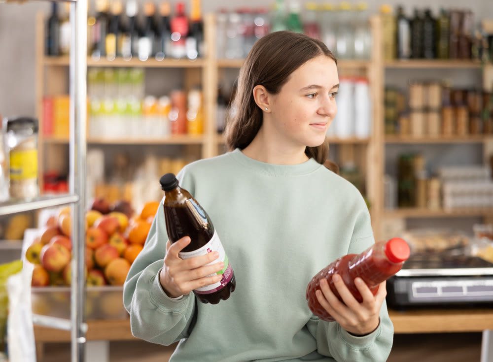 Teen girl hold packages bottles and choose consider juice in store