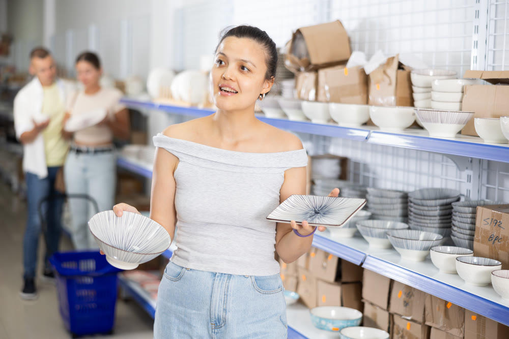 Positive Asian woman choosing plates in dishware store