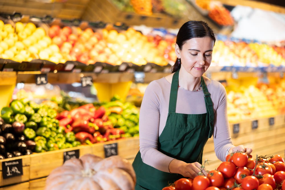 Supermarket employee carefully places ripe tomatoes on shelves of grocery supermarket