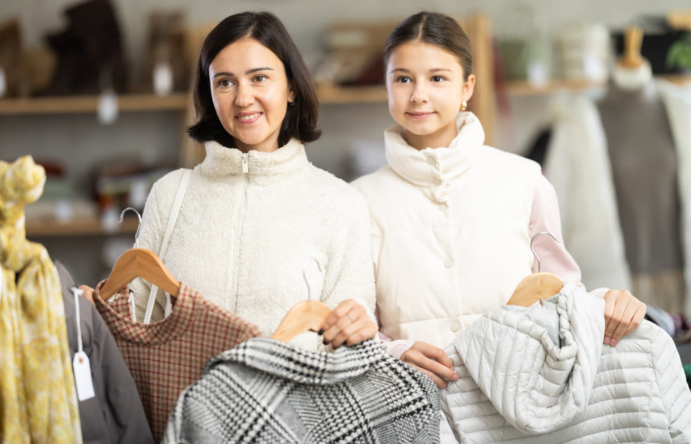 Mother and teen daughter looks at products in store and selects coat or jacket.
