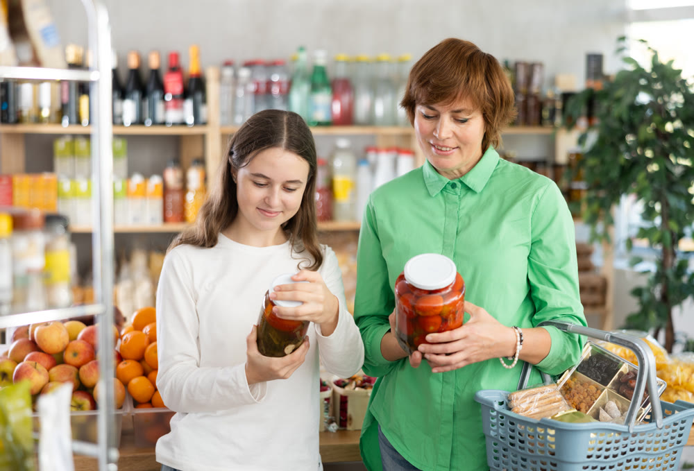Mother and daughter choose jar of pickled tomatoes together in grocery section of supermarket