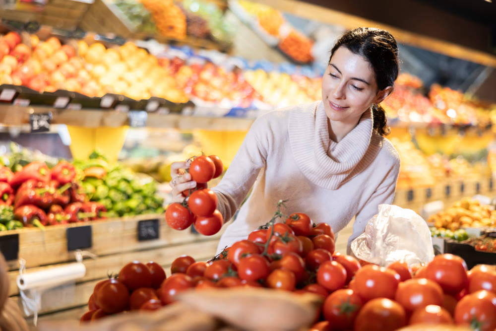 In vegetable store, young woman customer buy tomato