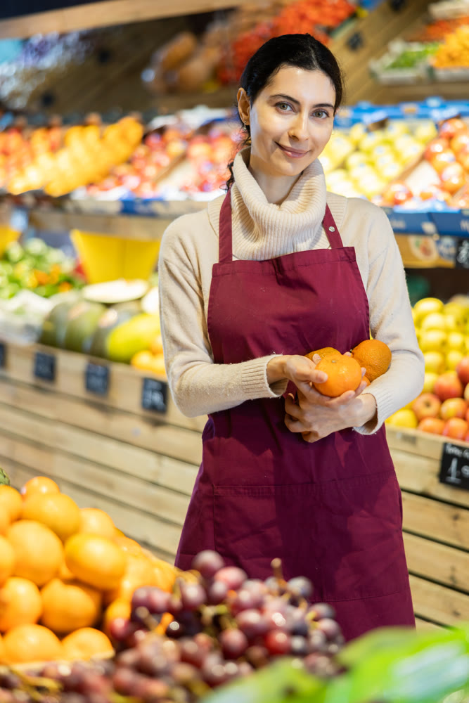 Woman staff with tangerine in hands in greengrocery