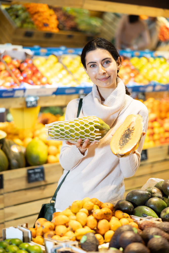 Young woman choosing papaya at vegetable shop