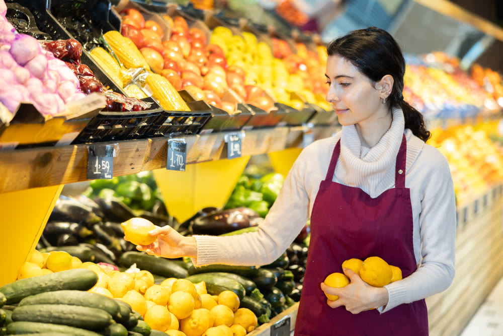 Young woman seller puts lemons in vegetable shop