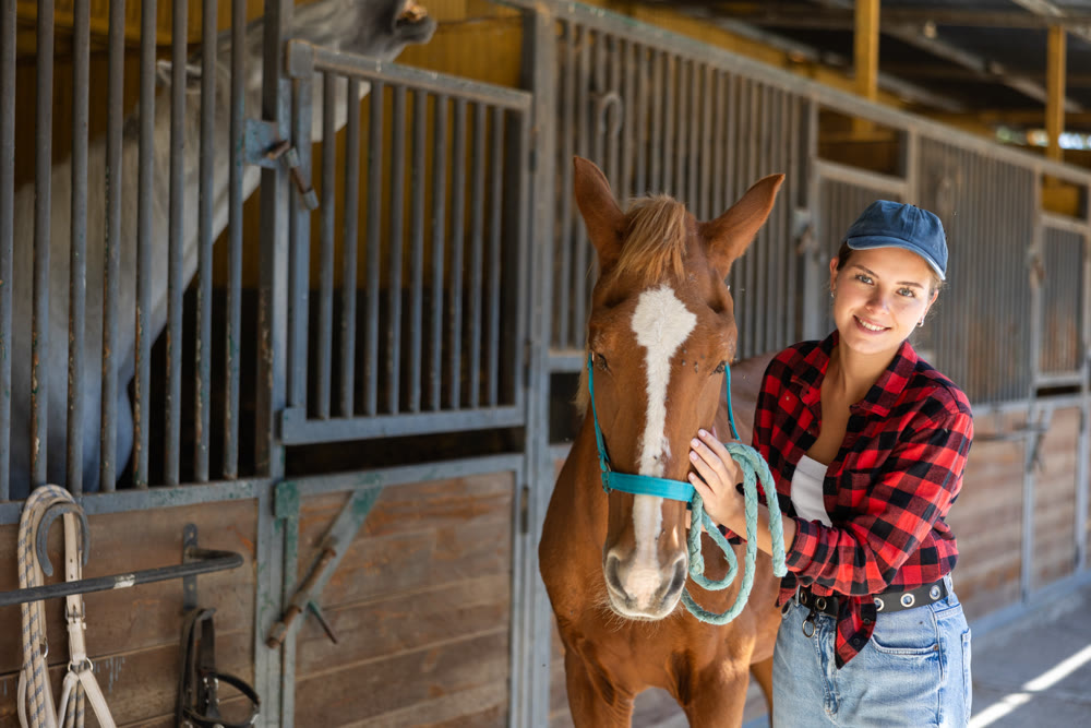 Young woman leads horse out of stable