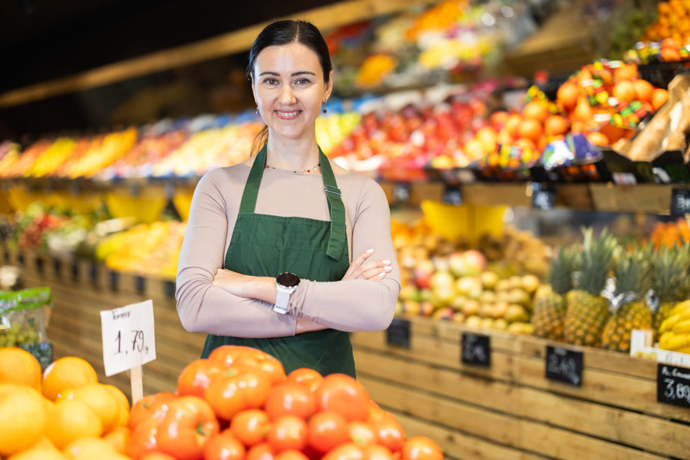 Supermarket employee carefully places ripe tomatoes on shelves of grocery supermarket
